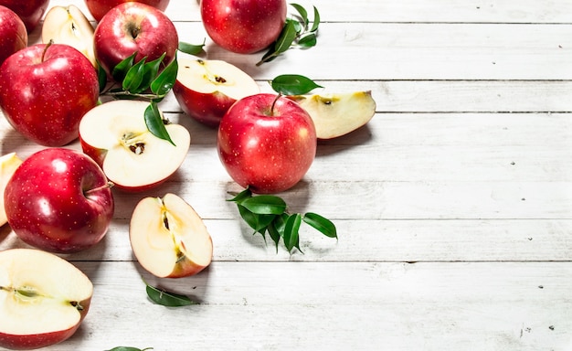 Fresh red apples with leaves on white wooden table.