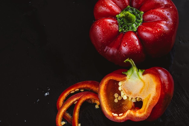 Fresh red bell pepper and slice on black background Top view Tropical abstract background Cloe up Pepper vegetaibles with drops of water