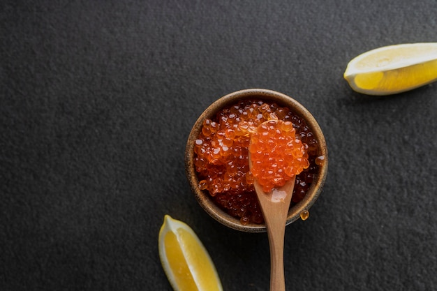 Fresh red caviar with a wooden spoon on a dark background in a ceramic bowl copyspace