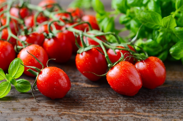 Fresh red cherry tomatoes with basil on a rustic wooden table.