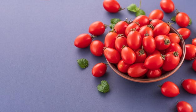 Fresh red cherry tomatoes in a wooden bowl isolated on a blue background, close up, copy space