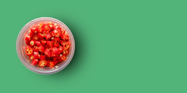 Fresh red chilli slides in a cup on a green background top view with copy space