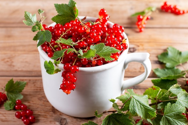 Fresh red currant berries in a cup on a wooden background Close up and selective focus