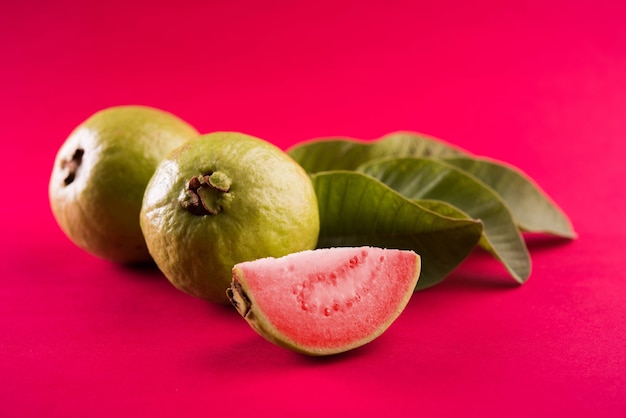 Photo fresh red guava fruit also known as amrood in hindi and peru in marathi, served in a basket as a whole or slices over colourful background. selective focus