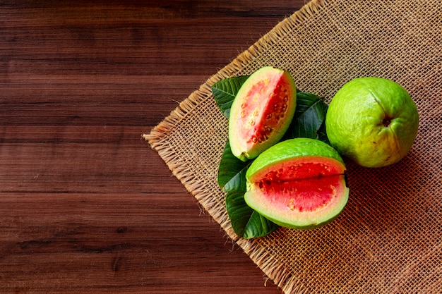 Fresh red guavas with green leaves on wooden table. Wood  and guava leaves.