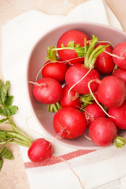 Fresh red radishes in a ceramic bowl over beige surface Closeup