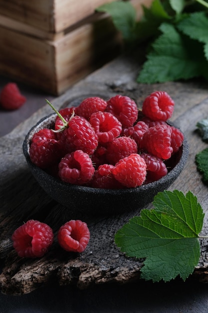 Fresh red raspberries in bowl on wooden dark table. Closeup berries background.