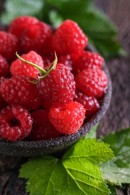 Fresh red raspberries in bowl on wooden dark table. Closeup berries background.