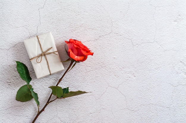 Fresh red rose and ecowrapped gift on gray texture background Top view