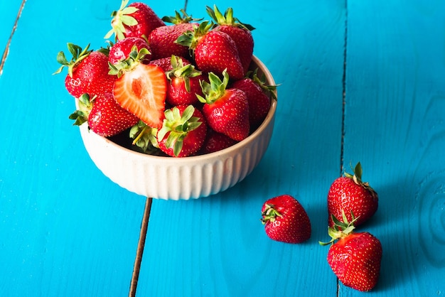 Fresh red strawberries in the bowl in blue wooden background Copy space top view