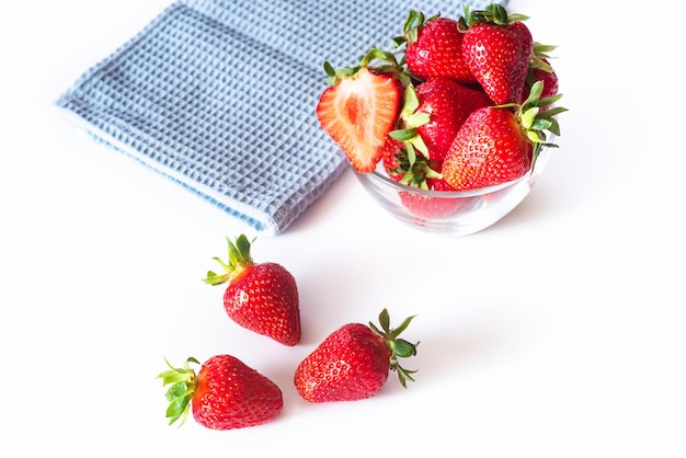 Fresh red strawberries in transparent bowl and small kitchen towel isolated on white background