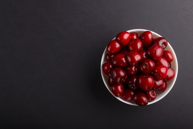 Fresh red sweet cherry in bowl on black background with copyspace. top view.