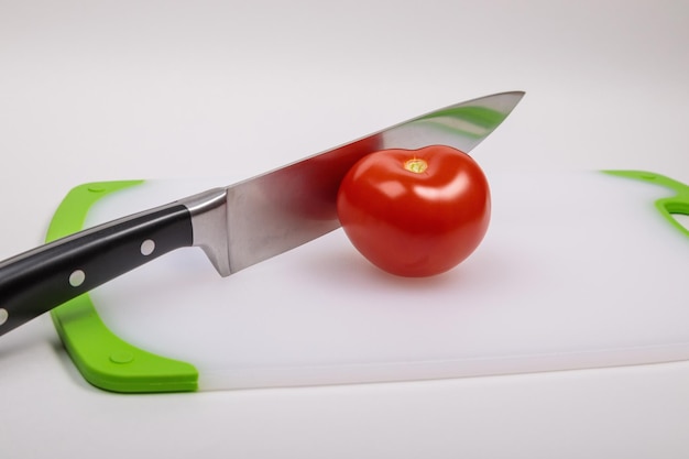 A fresh red tomato and a large chefs knife lie on a cutting board