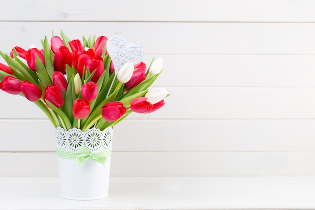 Fresh red tulip flowers bouquet on shelf in front of wooden wall.