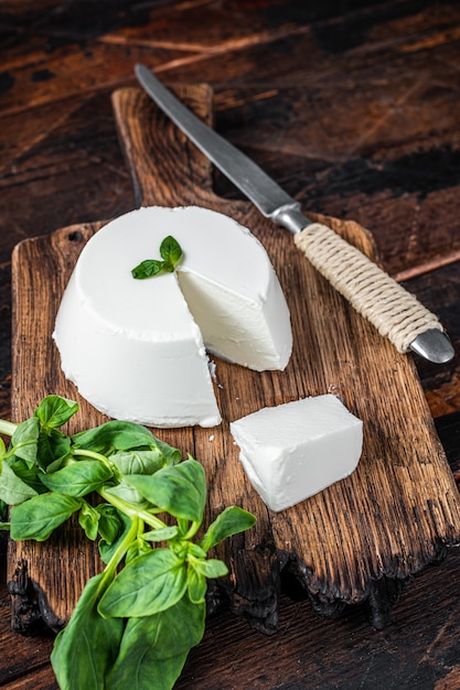 Photo fresh ricotta cream cheese on wooden board with basil. dark wooden background. top view.