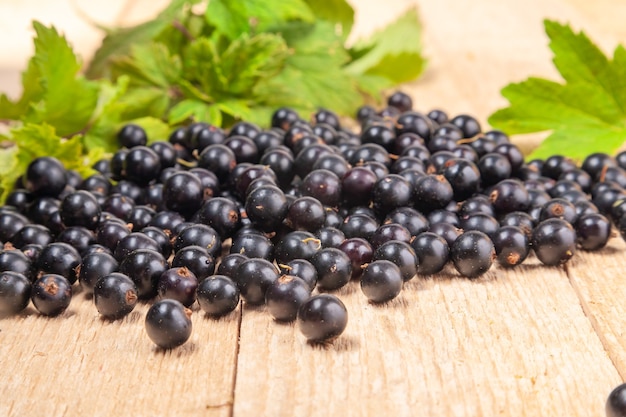 Fresh ripe black currants heap on wooden background. Natural organic berries with green leaves scattered on weathered wooden table, new berry harvest.