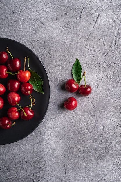 Photo fresh ripe cherry fruits with green leaves on black plate