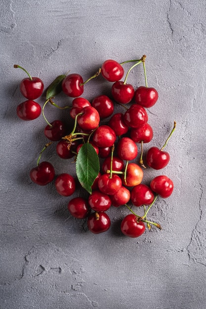 Fresh ripe cherry fruits with green leaves, summer vitamin berries on grey stone