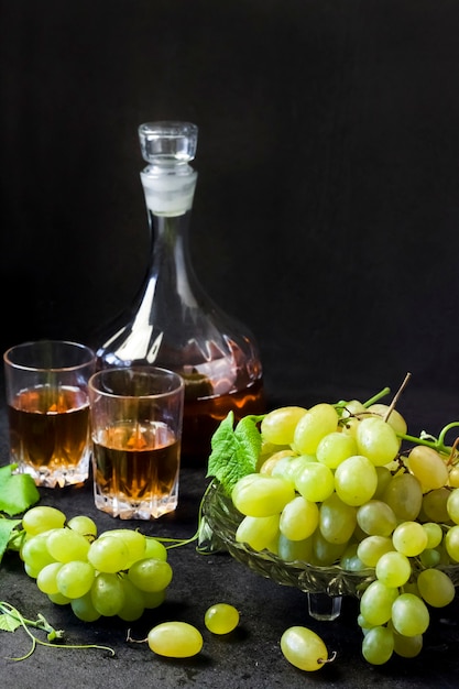 Fresh ripe grapes in a fruit bowl and decanter and two glasses with grape juice on black background