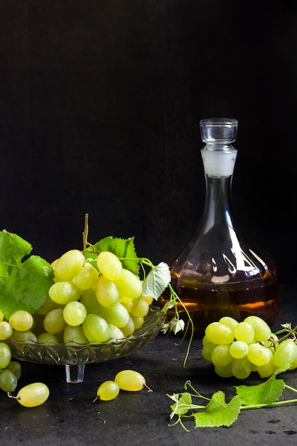 Fresh ripe grapes in a fruit bowl and decanter with grape juice  on black background