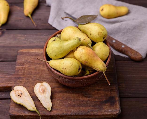 Fresh ripe green pears in a brown clay bowl on a table, top view