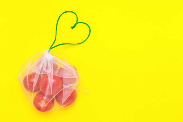 Fresh ripe and juicy tomatoes in reusable eco-friendly mesh bag on the yellow.