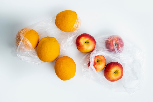 Fresh ripe oranges apples in transparent plastic bags on a white background Top view flat lay