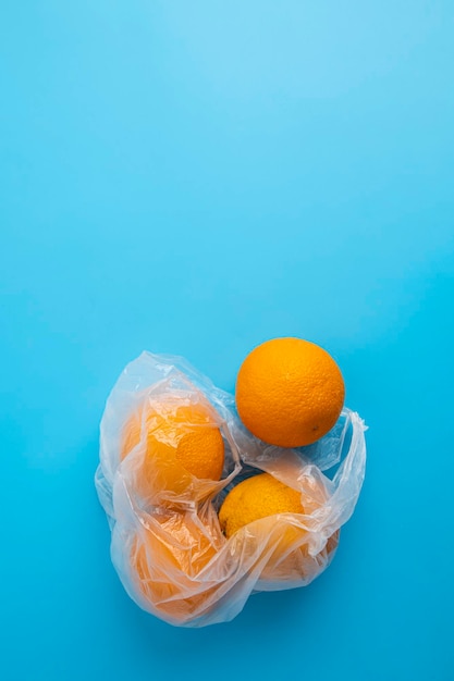 Fresh ripe oranges in a transparent plastic bag on a blue background Top view flat lay