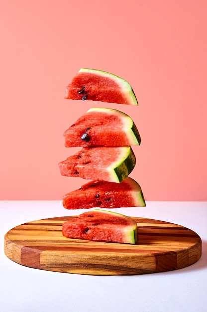 Fresh ripe pieces watermelon flying over wooden board on pink background Creative minimal concept