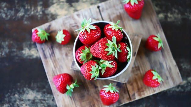 Fresh ripe strawberries in a bowl and on a wooden surface.