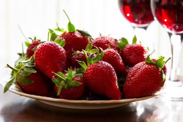 Fresh ripe strawberries and glasses of red wine in the background