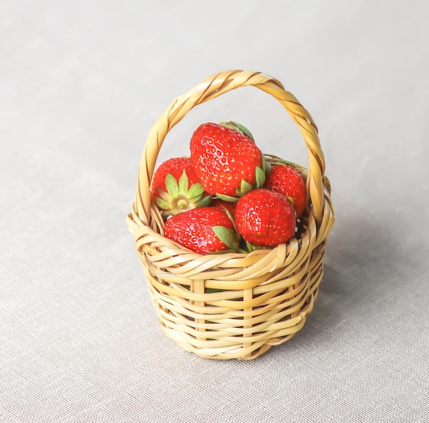 Fresh ripe strawberries in the small wicker basket on linen tablecloth