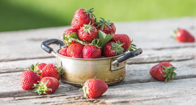 Fresh ripe strawberries in vintage kitchen pot on old garden table.