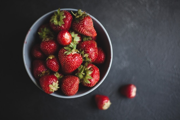 Fresh ripe tasty strawberries in a black plate on a gray wooden background. Two bast bins lie side by side.