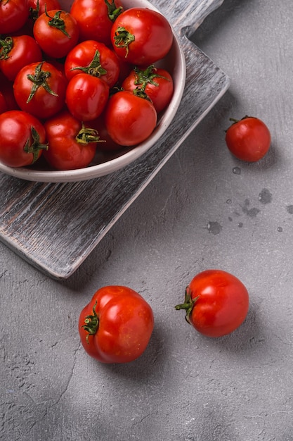 Fresh ripe tomatoes with water drops in bowl on old wooden cutting board