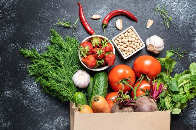 Fresh ripe vegetables, fruit and greens in craft paper shopping bag on black rustic background