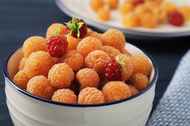 Fresh ripe yellow raspberries in bowl on blue wooden background