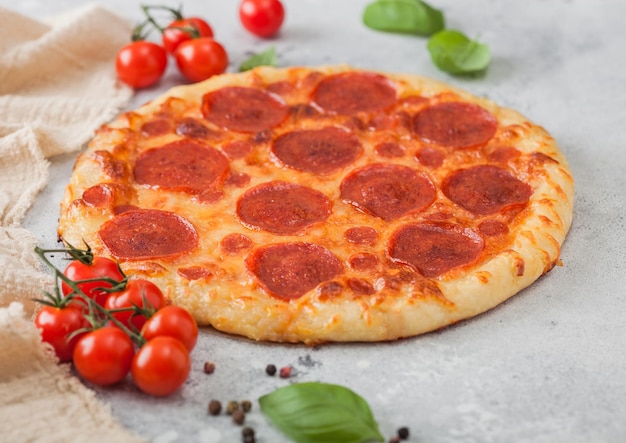 Fresh round baked Pepperoni italian pizza with tomatoes with basil on light kitchen table background Space for text