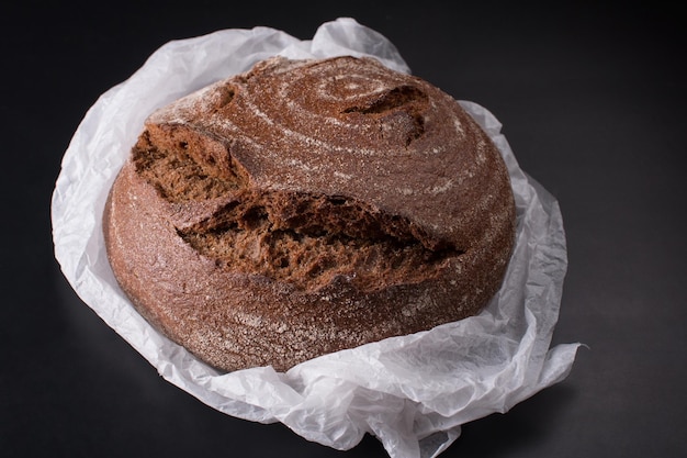 Fresh round black bread with a crispy crust Closeup on a black background