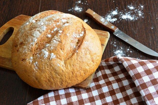 fresh round bread on the cutting board with  towel and kitchen knife on the wooden table