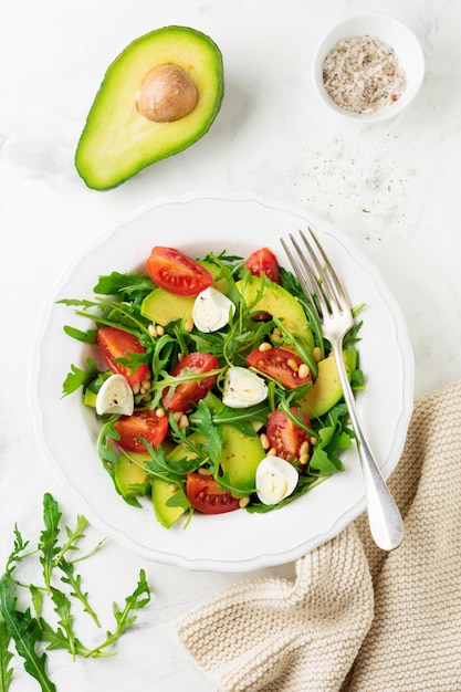 Fresh salad from arugula, tomato, avocado, olive oil, nuts and quail eggs on a light stone background