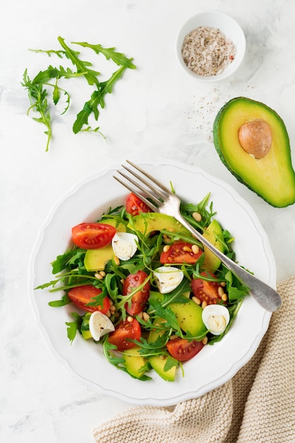 Fresh salad from arugula, tomato, avocado, olive oil, nuts and quail eggs