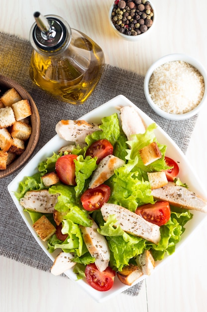 Fresh salad made of tomato, ruccola, chicken breast, eggs, arugula, crackers and spices. Caesar salad in a white, transparent bowl on wooden background