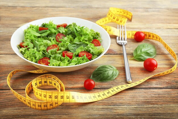 Fresh salad and measuring tape on wooden background