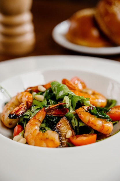 Fresh salad plate with shrimp, tomato and mixed greens on wooden surface close up