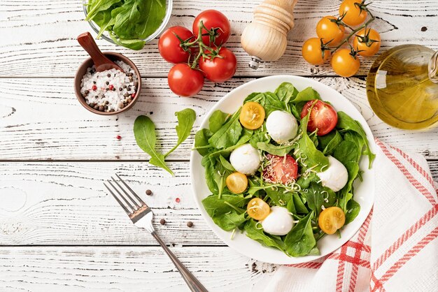 Fresh salad with arugula cherry tomatoes mozzarella cheese and hard cheese on white wooden background Top view