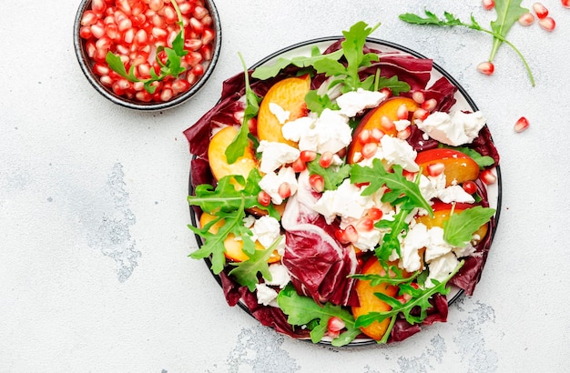 Fresh salad with arugula radicchio sweet peaches feta cheese and pomegranate seeds White table background top view