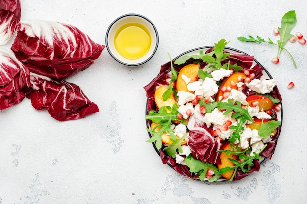 Fresh salad with arugula radicchio sweet peaches feta cheese and pomegranate seeds White table background top view