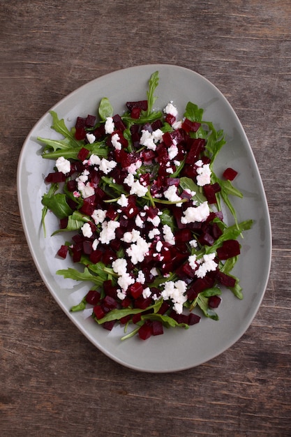 Fresh salad with beetroot, arugula and feta cheese in a plate on a dark background, top view.