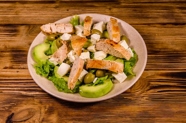 Fresh salad with chicken meat feta cheese avocado green olives and lettuce leaves in ceramic plate on wooden table